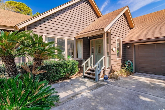 doorway to property featuring a garage, driveway, and a shingled roof