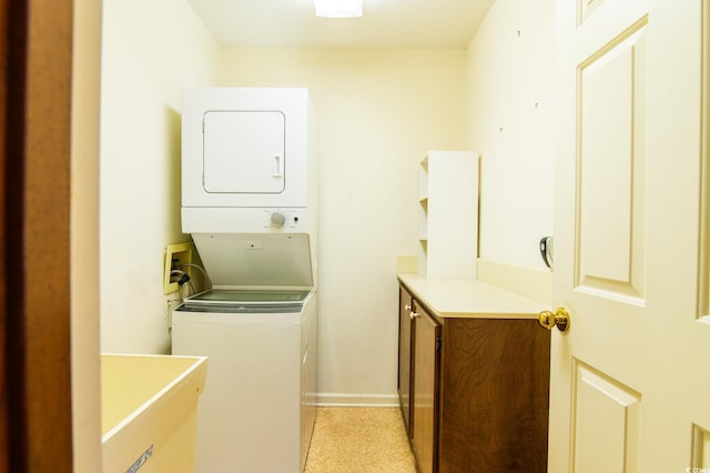 laundry area with stacked washer / dryer, cabinet space, and baseboards