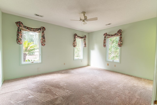 carpeted empty room featuring baseboards, visible vents, a textured ceiling, and a ceiling fan