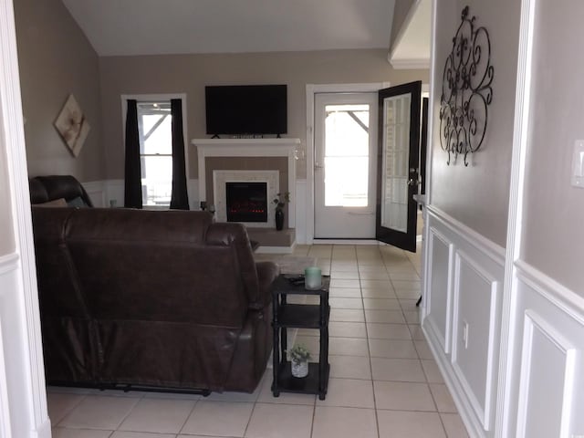 living room featuring plenty of natural light, a wainscoted wall, and a warm lit fireplace