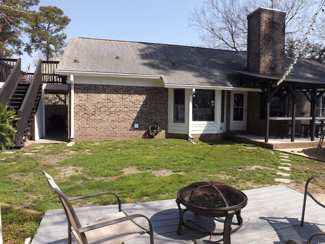 back of property with brick siding, stairway, an outdoor fire pit, a yard, and a deck