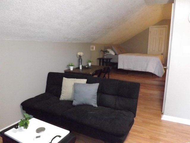 living room with light wood-type flooring, baseboards, a textured ceiling, and vaulted ceiling