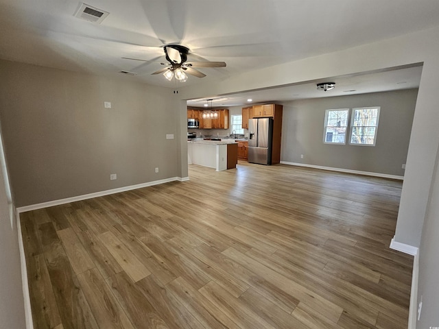 unfurnished living room with light wood finished floors, visible vents, baseboards, and ceiling fan