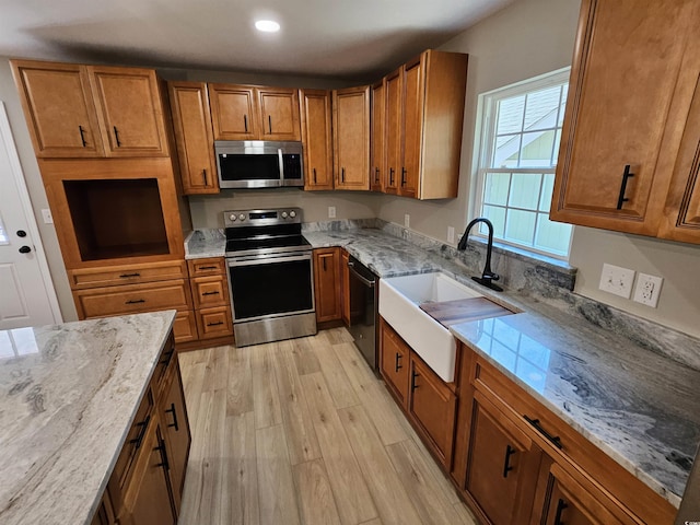 kitchen with light stone counters, a sink, light wood-style floors, appliances with stainless steel finishes, and brown cabinets