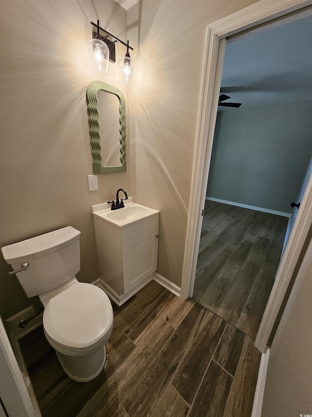 half bathroom with vanity, wood finished floors, baseboards, ceiling fan, and toilet