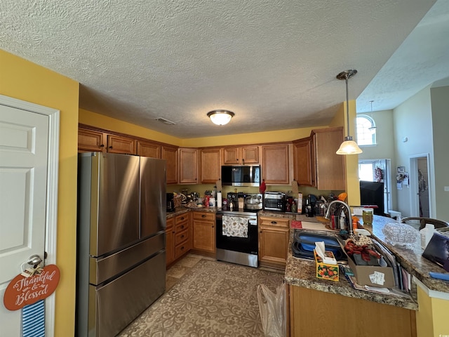 kitchen featuring brown cabinetry, a peninsula, a sink, appliances with stainless steel finishes, and pendant lighting