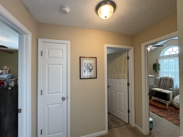 hall featuring baseboards, carpet, and a textured ceiling