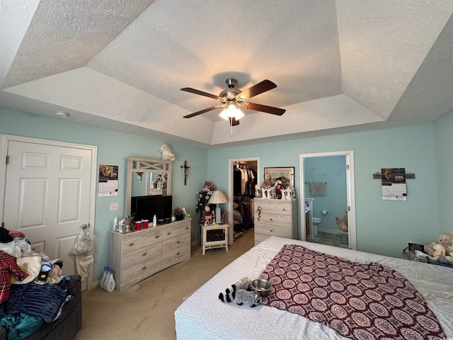 bedroom with a textured ceiling, a tray ceiling, a spacious closet, and light carpet