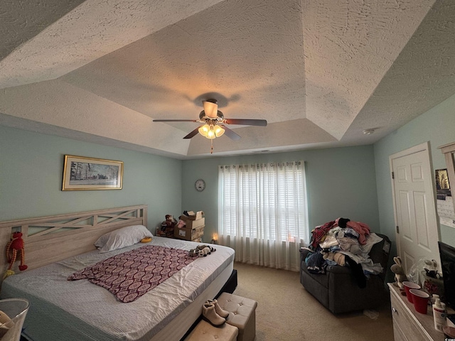 bedroom with a ceiling fan, a tray ceiling, light colored carpet, and a textured ceiling