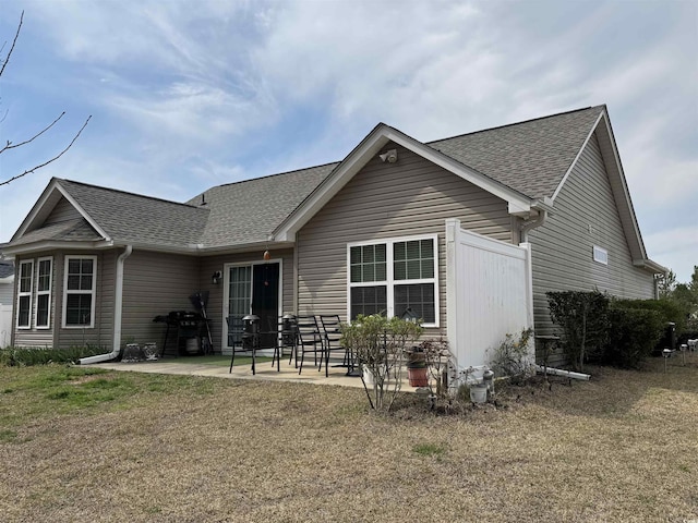 back of property with a yard, a patio, and a shingled roof