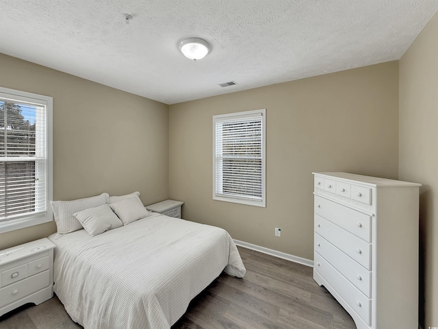 bedroom with a textured ceiling, wood finished floors, visible vents, and baseboards