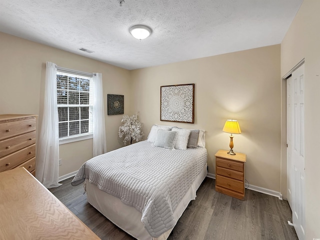 bedroom with visible vents, a closet, baseboards, a textured ceiling, and dark wood finished floors