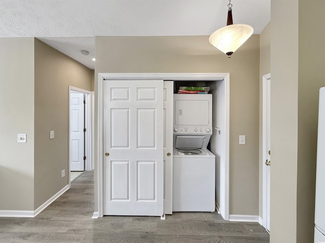 washroom with wood finished floors, baseboards, laundry area, stacked washer and dryer, and a textured ceiling