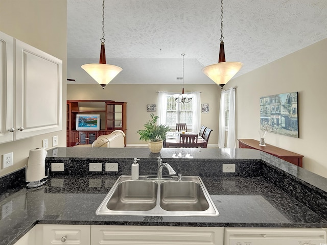kitchen with white cabinets, a textured ceiling, a chandelier, and a sink