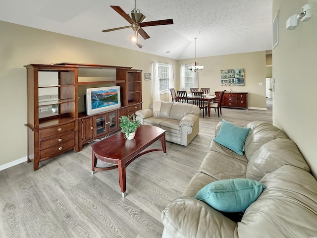 living area with baseboards, lofted ceiling, light wood-style floors, a textured ceiling, and ceiling fan with notable chandelier