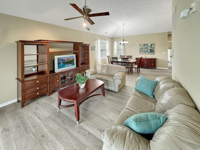 living room with light wood finished floors, a textured ceiling, ceiling fan with notable chandelier, lofted ceiling, and visible vents
