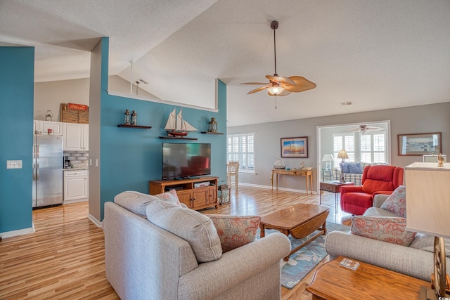 living room featuring a ceiling fan, baseboards, vaulted ceiling, a textured ceiling, and light wood-type flooring