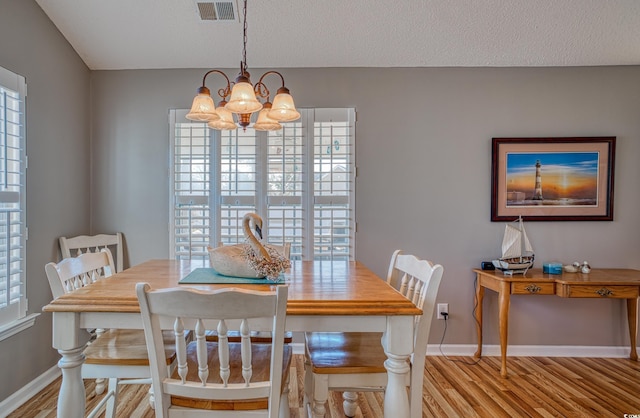 dining area with visible vents, light wood finished floors, an inviting chandelier, and a healthy amount of sunlight