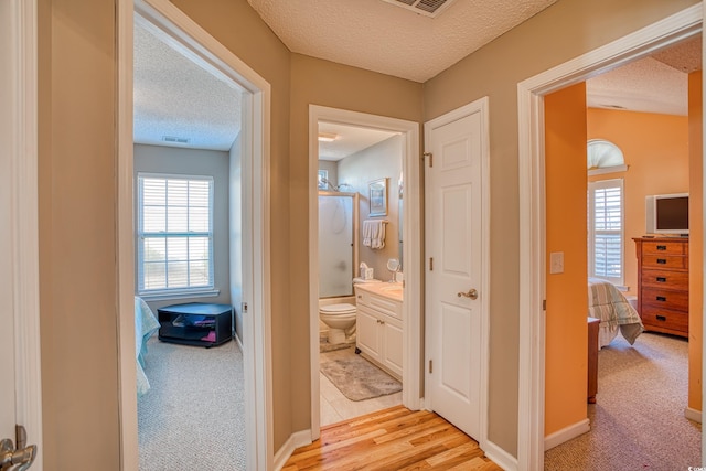 hall with visible vents, a textured ceiling, and light colored carpet