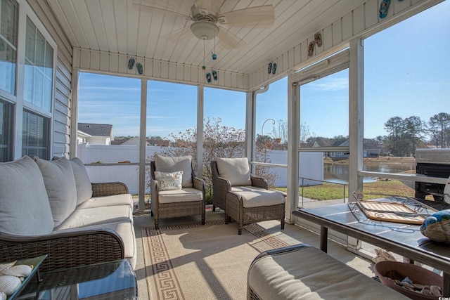 sunroom with ceiling fan and a water view