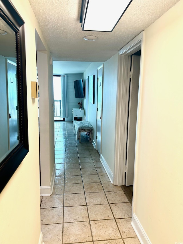 hallway with light tile patterned floors, baseboards, and a textured ceiling