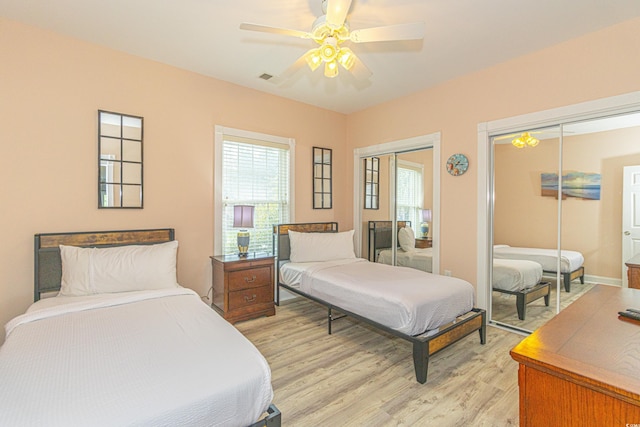 bedroom featuring multiple windows, a ceiling fan, light wood-type flooring, and two closets