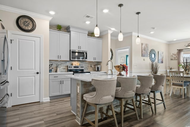 kitchen with a breakfast bar area, a center island with sink, a sink, appliances with stainless steel finishes, and crown molding