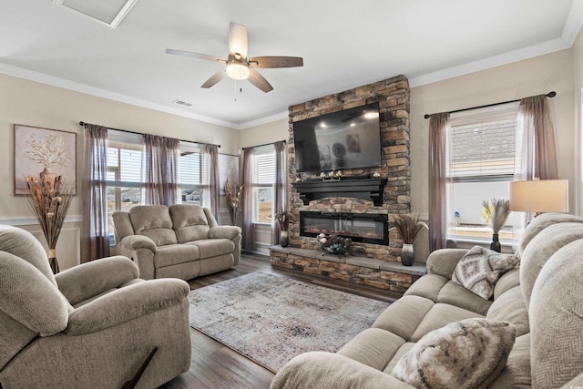 living room with a stone fireplace, crown molding, wood finished floors, and ceiling fan