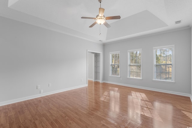 empty room featuring light wood finished floors, visible vents, a raised ceiling, and ceiling fan