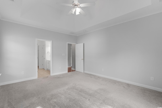 unfurnished bedroom featuring light carpet, a tray ceiling, connected bathroom, crown molding, and baseboards