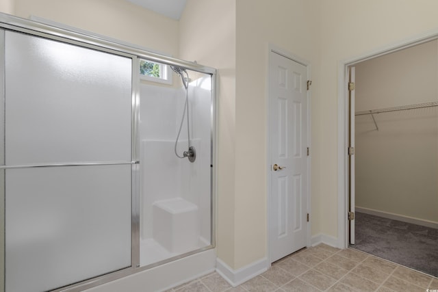 bathroom featuring a walk in closet, a shower stall, and baseboards