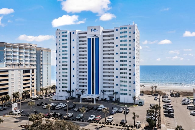 view of building exterior with a water view, uncovered parking, and a view of the beach