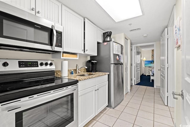 kitchen featuring light tile patterned floors, appliances with stainless steel finishes, white cabinetry, and a sink