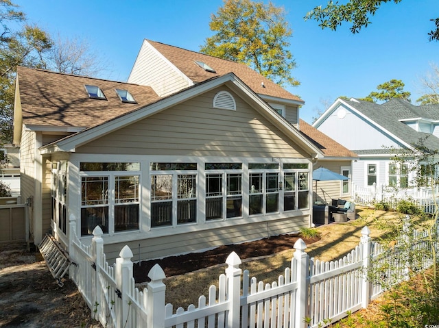 rear view of property with a fenced front yard, a sunroom, and a shingled roof