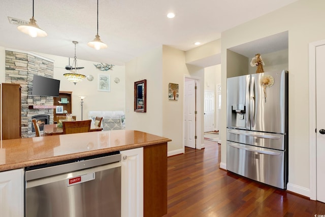 kitchen with dark wood finished floors, a stone fireplace, hanging light fixtures, appliances with stainless steel finishes, and white cabinetry