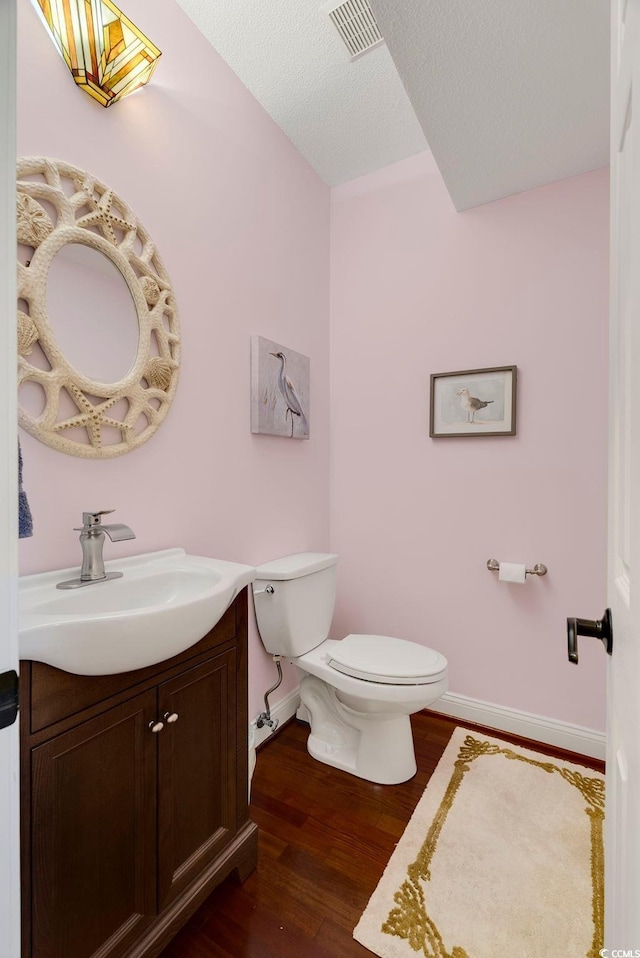 half bathroom with visible vents, baseboards, toilet, wood finished floors, and vanity