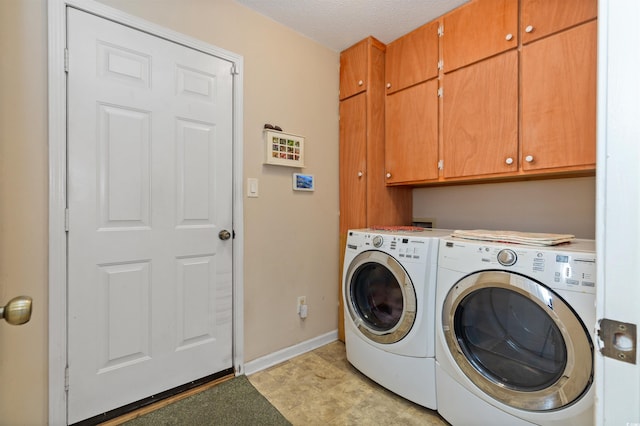 laundry area featuring washing machine and dryer, cabinet space, a textured ceiling, and baseboards