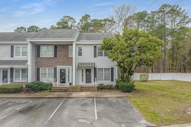 view of property featuring uncovered parking, roof with shingles, a front yard, and fence