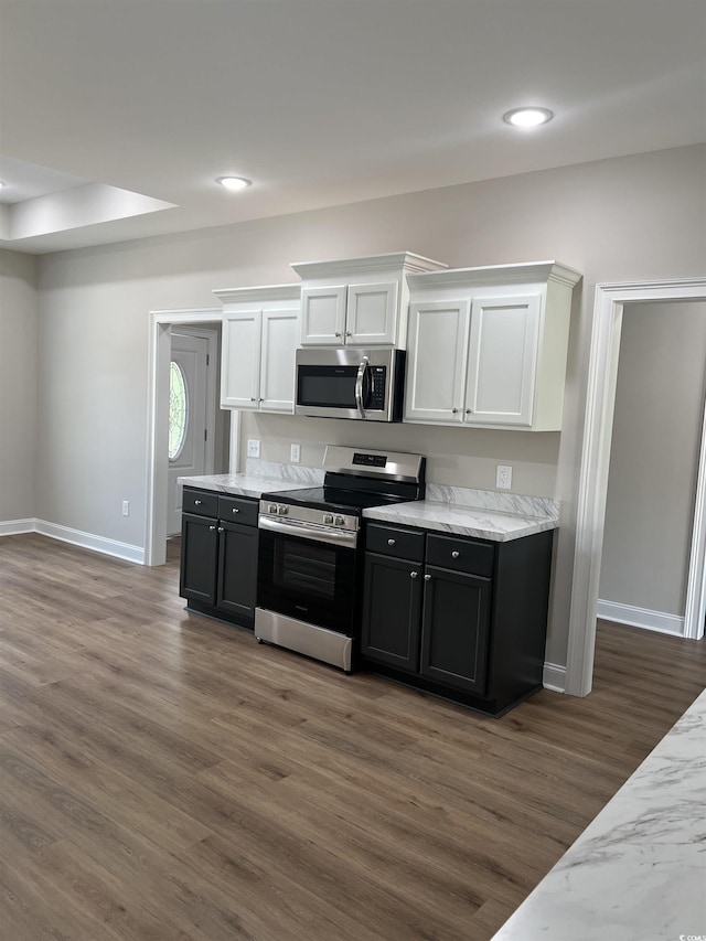 kitchen featuring dark wood-style flooring, appliances with stainless steel finishes, light stone counters, white cabinetry, and baseboards