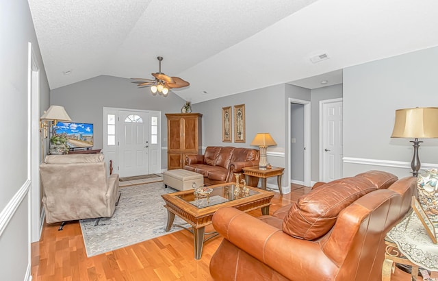 living room featuring a ceiling fan, visible vents, lofted ceiling, a textured ceiling, and light wood-type flooring