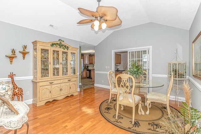 dining area featuring a ceiling fan, visible vents, light wood finished floors, baseboards, and lofted ceiling