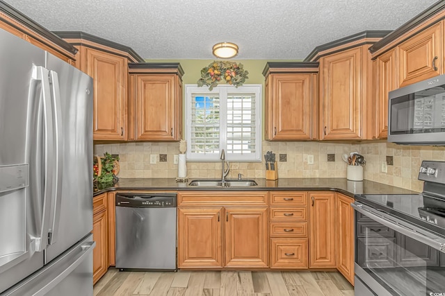 kitchen featuring dark countertops, light wood finished floors, appliances with stainless steel finishes, brown cabinetry, and a sink