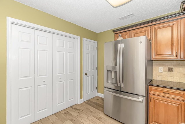 kitchen with dark countertops, stainless steel fridge with ice dispenser, brown cabinets, and light wood-type flooring