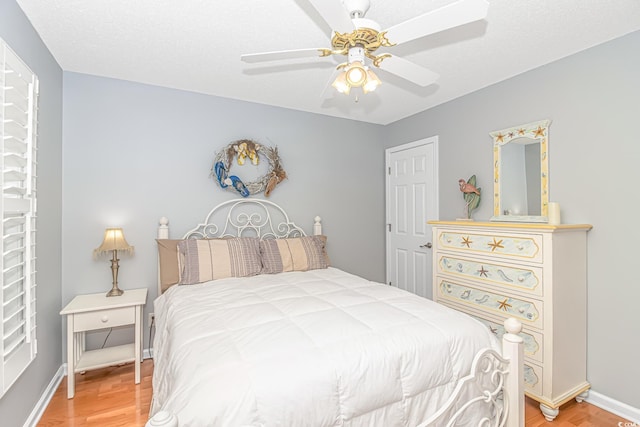 bedroom featuring light wood-style flooring, a textured ceiling, baseboards, and ceiling fan