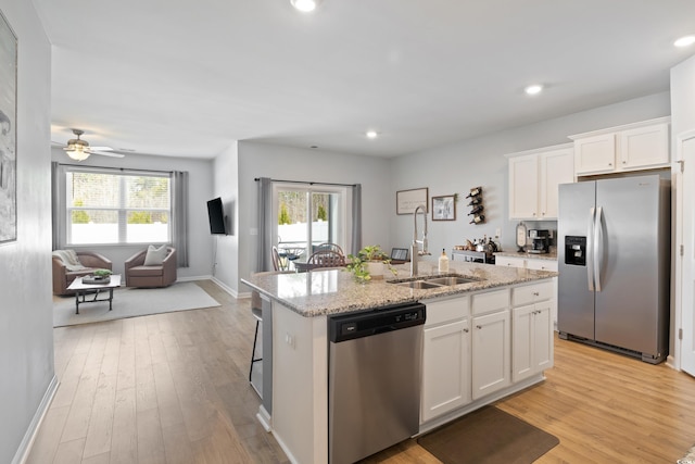 kitchen with appliances with stainless steel finishes, a sink, open floor plan, light wood-style flooring, and light stone countertops