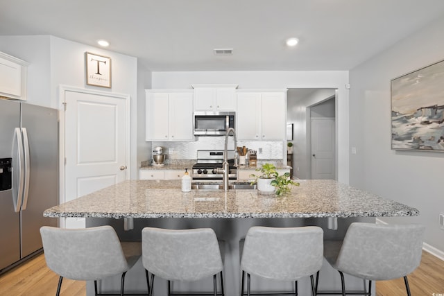 kitchen with appliances with stainless steel finishes, a sink, white cabinetry, a kitchen bar, and recessed lighting