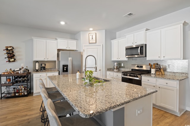 kitchen featuring appliances with stainless steel finishes, a sink, an island with sink, a kitchen bar, and light wood-type flooring