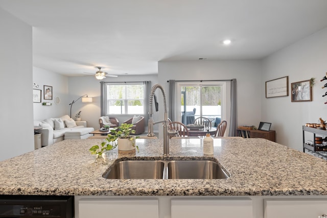 kitchen featuring a sink, open floor plan, dishwashing machine, light stone countertops, and a ceiling fan
