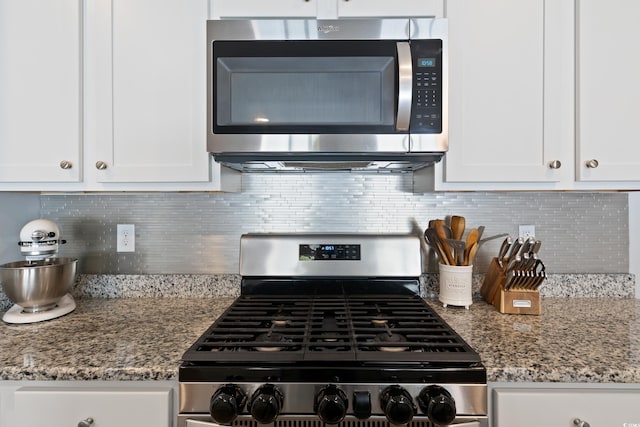 kitchen featuring stainless steel appliances, white cabinetry, light stone counters, and decorative backsplash