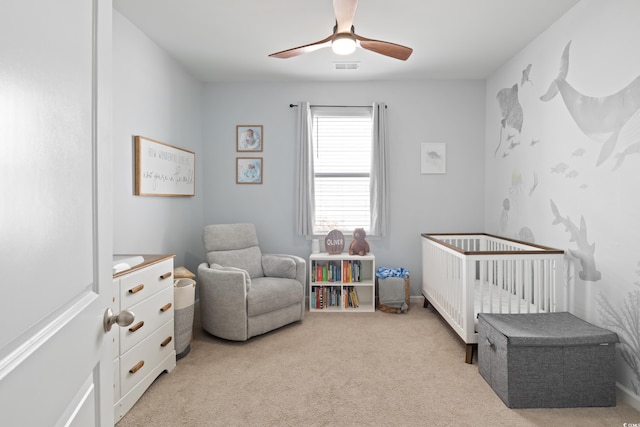 bedroom featuring light carpet, a crib, and a ceiling fan